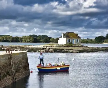 A Saint-Cado, la fameuse petite maison aux volets bleus posée sur l'îlot rocheux de Nichtarguer, surnommée aussi la maison de l'huître avec un pécheur prêt à partir.