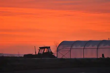 tracteur et serre à l'aube ciel rouge orange campagne travail des champs