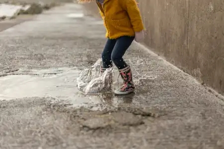 Une petite fille saute avec ses bottes dans un flaque dos sur une digue