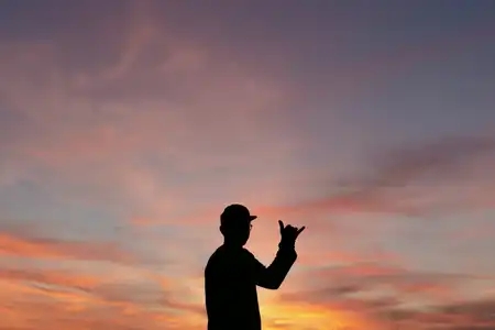 la silhouette d'un jeune homme avec casquette fait un signe shaka devant un magnifique coucher de soleil