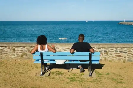 Une jeune fille et un jeune homme pique-nique assis sur un banc de dos face à la mer