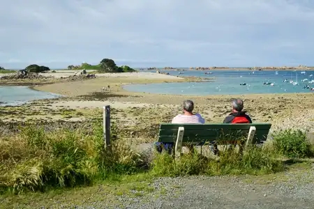 Deux hommes assis sur un banc de dos face à la mer à marée basse