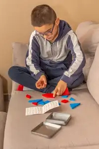 garçon jouant à un tangram en bois coloré sur un canapé