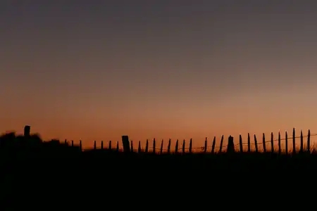 Une barrière délimitant la dune se distingue contre le ciel dégradé du coucher de soleil