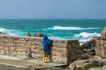 Enfant voulant regarder les vagues par dessus un muret