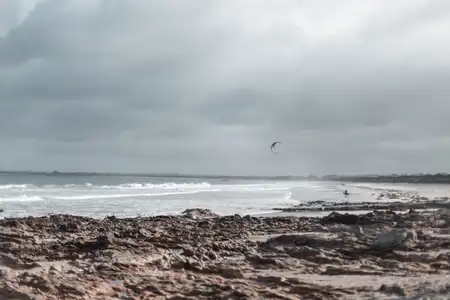 Un kitesufer s'apprête à entrer dans l'eau sous un ciel gris de tempête