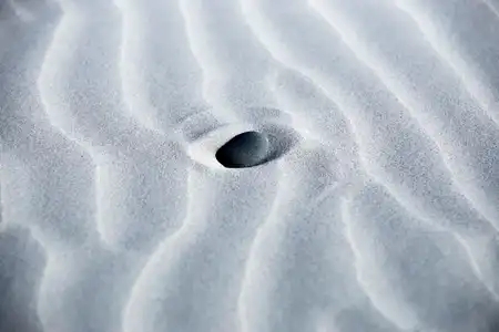 Un galet noir posé sur le sable blanc de la plage de Porzh Karn