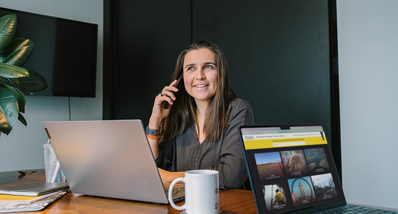 Une femme assise à un bureau avec un ordinateur portable et parlant au téléphone.