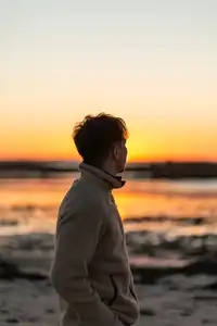 Un jeune homme contemple le coucher du soleil sur une plage du Finistère