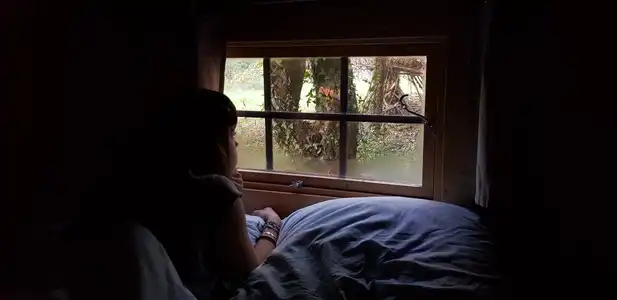 Jeune fille allongée, dans la pénombre, regardant par la fenêtre