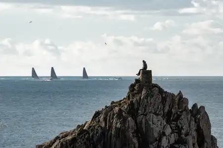 un homme sur un rocher regarde le départ de voiliers